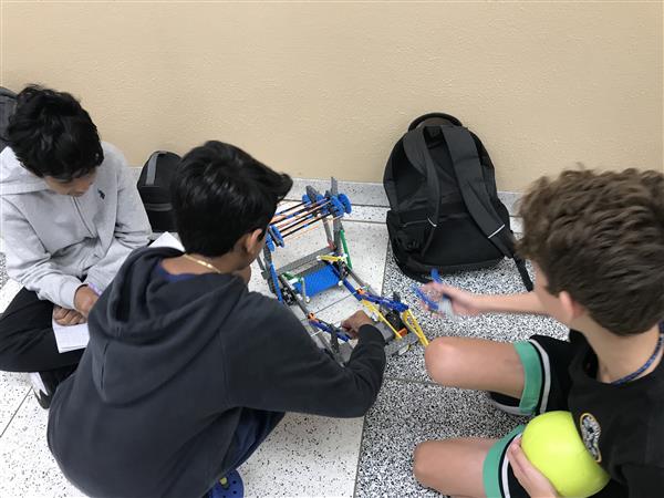 A group of three students works on a robot at practice.